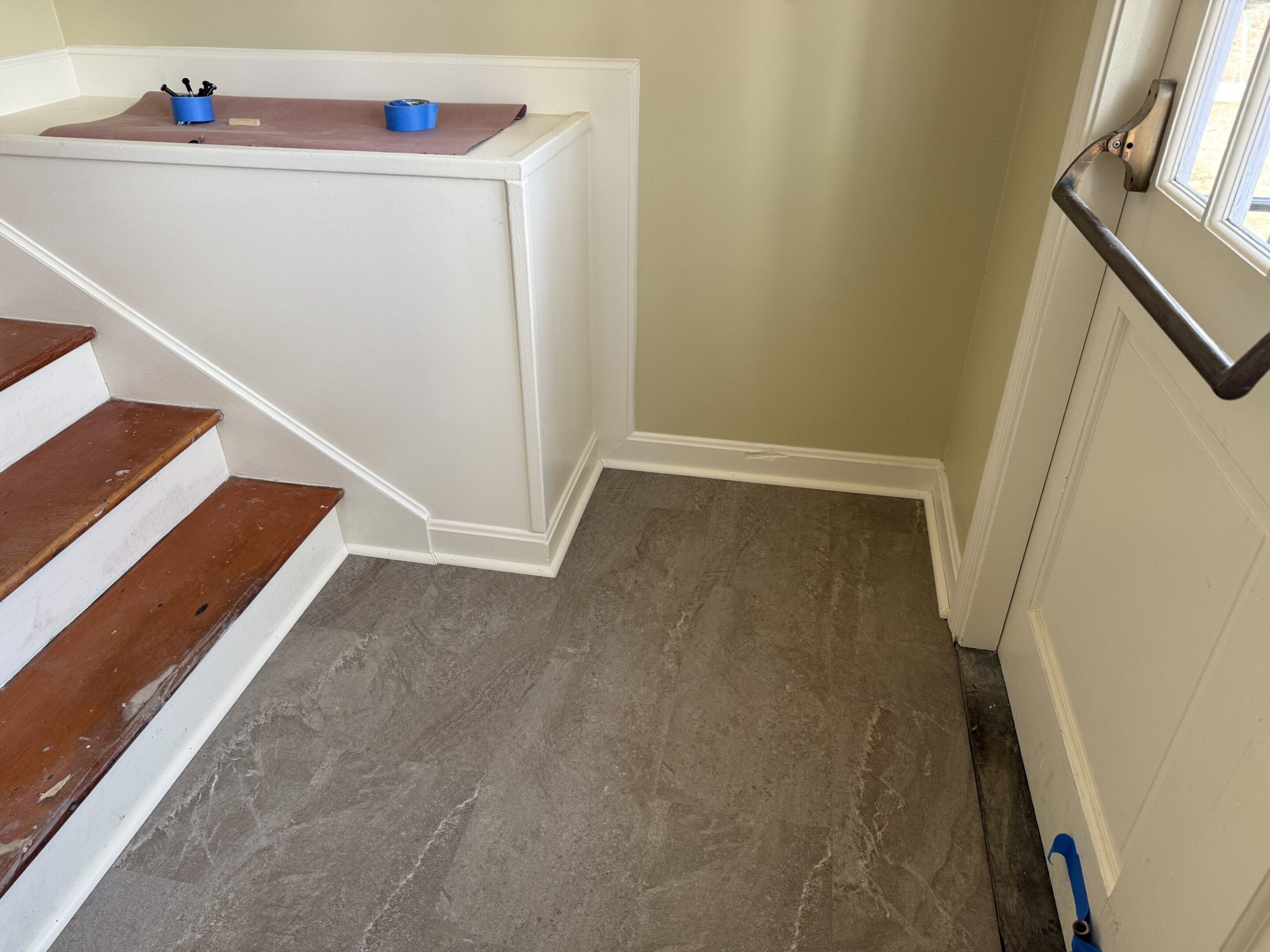 Newly installed gray tile flooring near a staircase and wall corner.