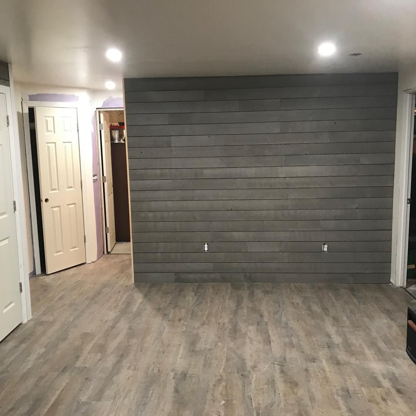 Empty room with gray wood flooring and dark accent wall.