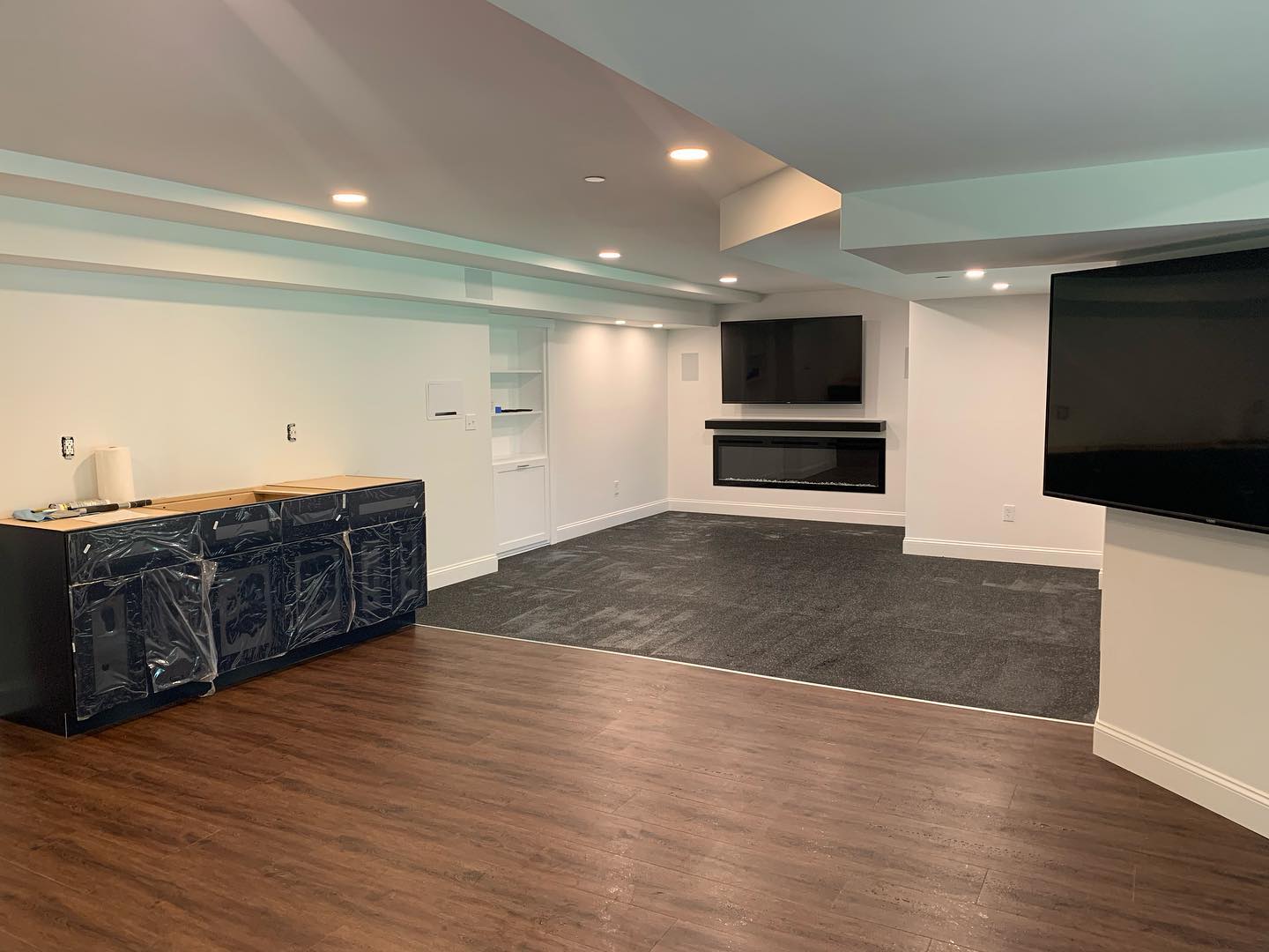Modern basement with hardwood floors, built-in fireplace, and dark carpeted area.