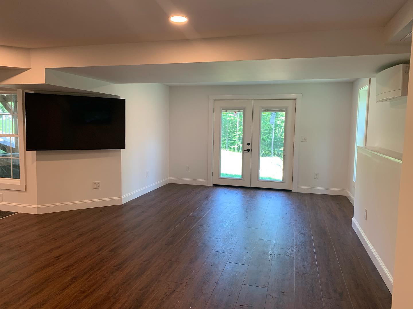 Spacious empty room with wooden floors and French doors.