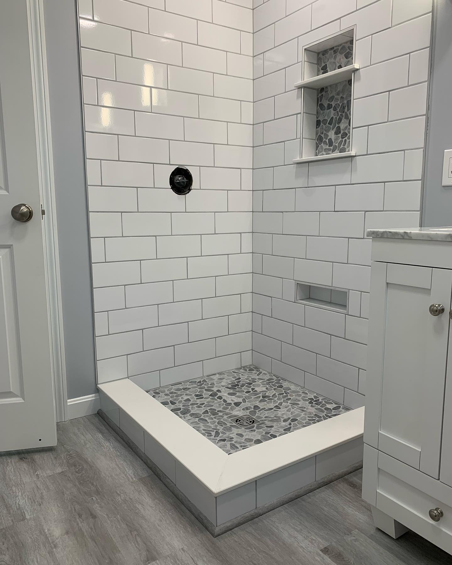 A small shower with white subway tiles and a marble floor.