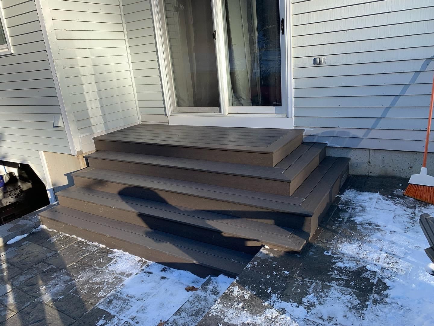 Stacked wooden steps leaning against a white building in winter.