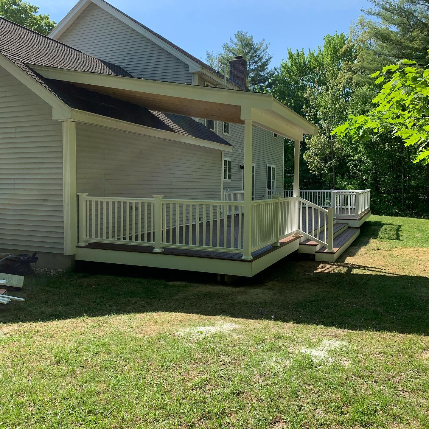 A white house with a covered porch and wooden deck in a sunny yard.