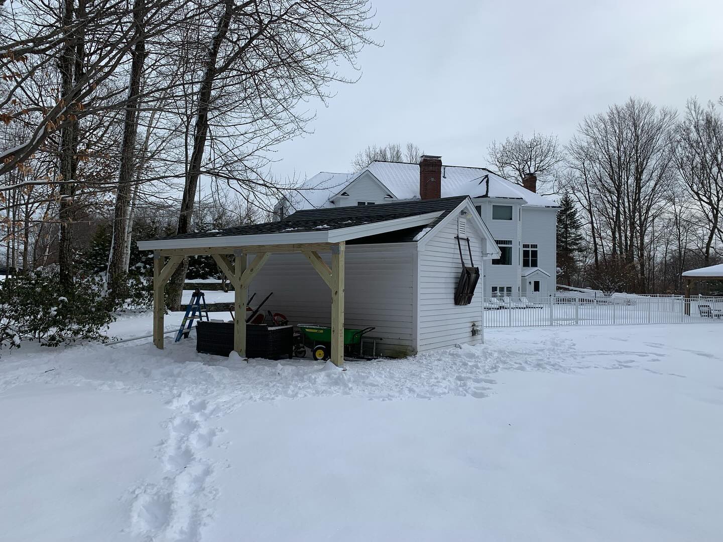 Snow-covered house with a carport and footprints in the snow.