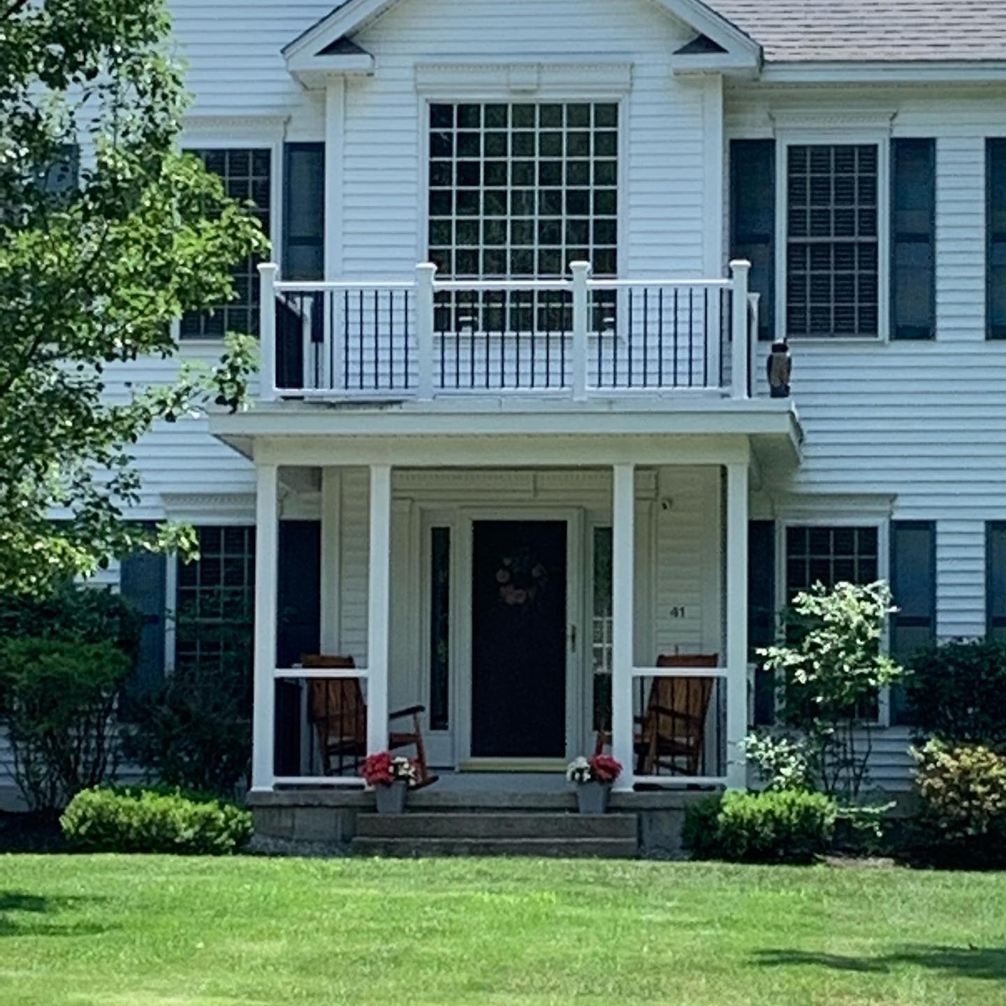 White two-story house with a porch and rocking chairs.