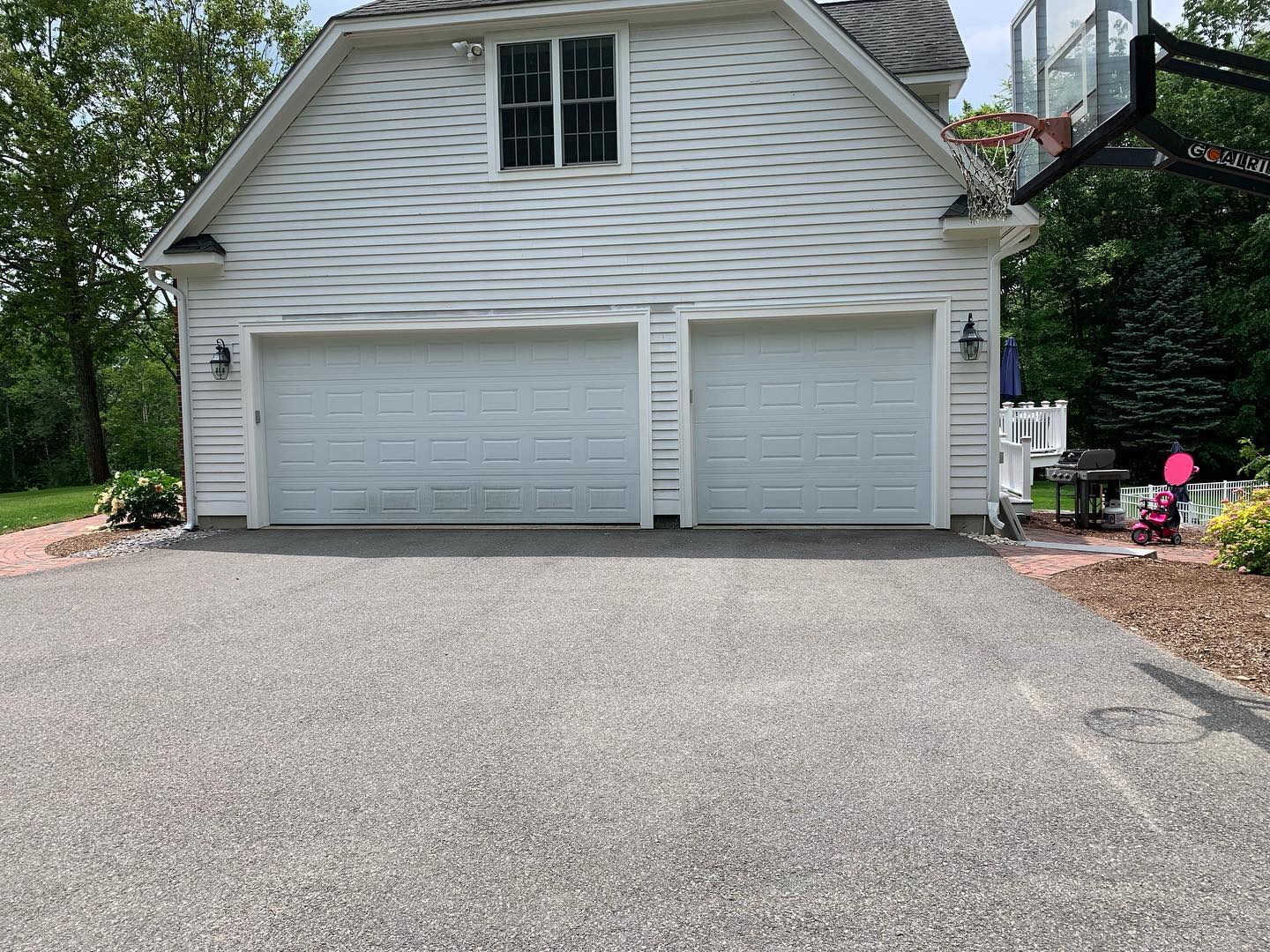 Two white garage doors on a residential house with a paved driveway.