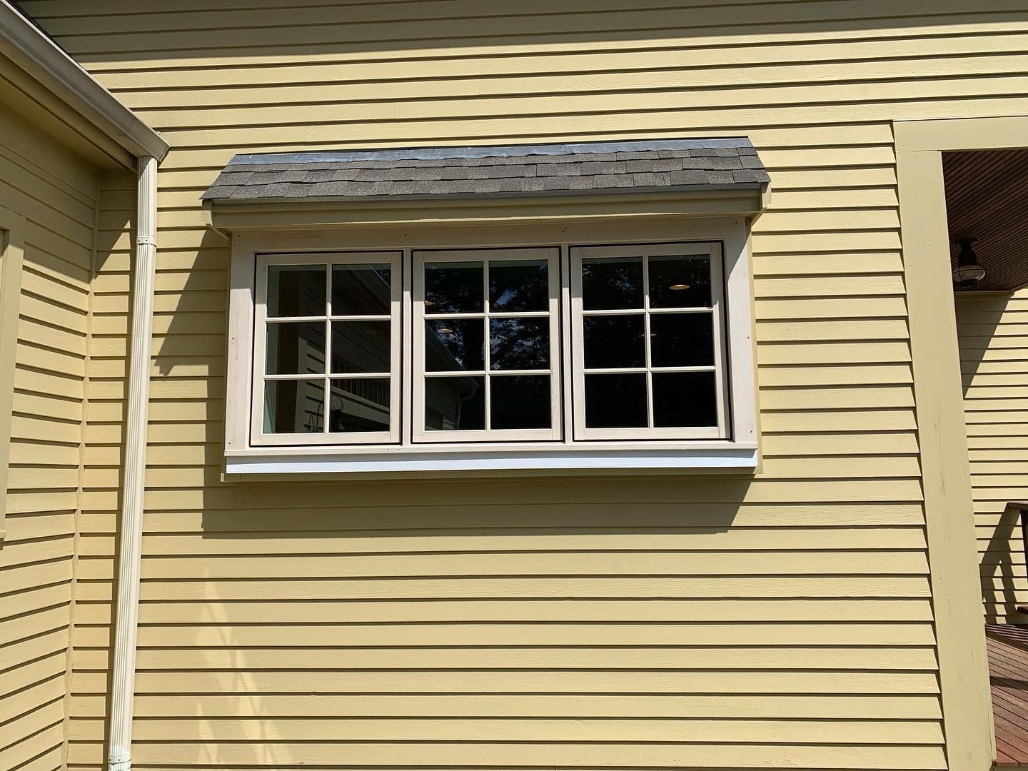 White window with awning on yellow house siding.