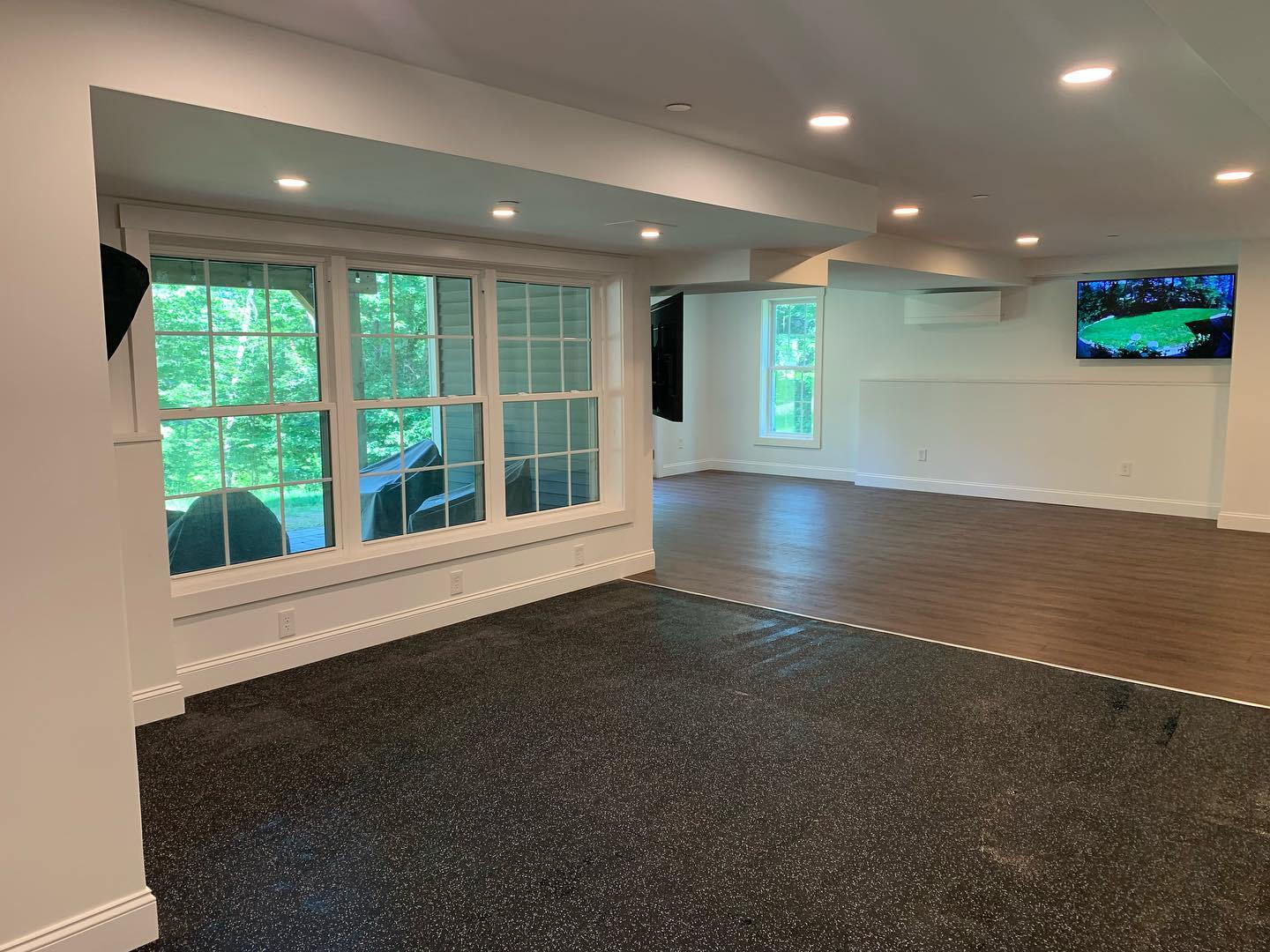 Empty room with large windows and mixed flooring.