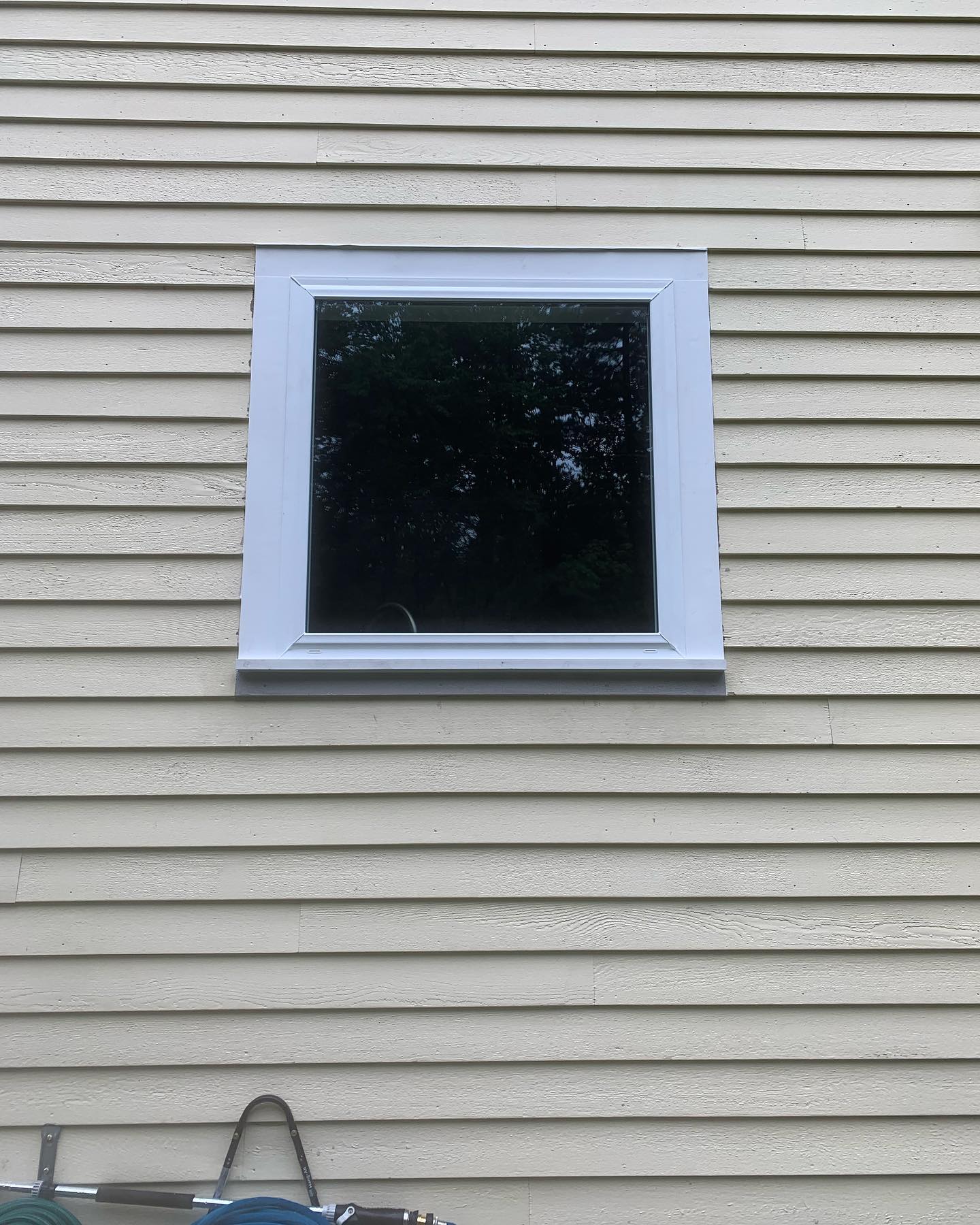 A single black-framed window on beige siding wall.