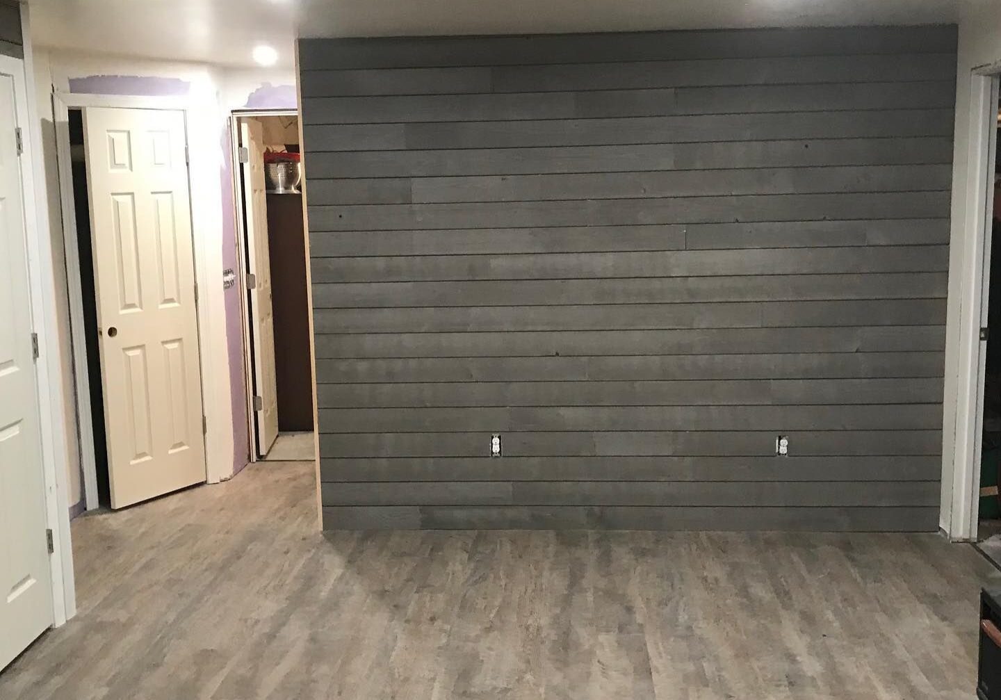 Empty room with gray wood floor and dark accent wall.