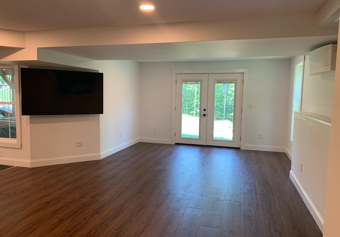 Spacious empty room with wooden floors and double glass doors.