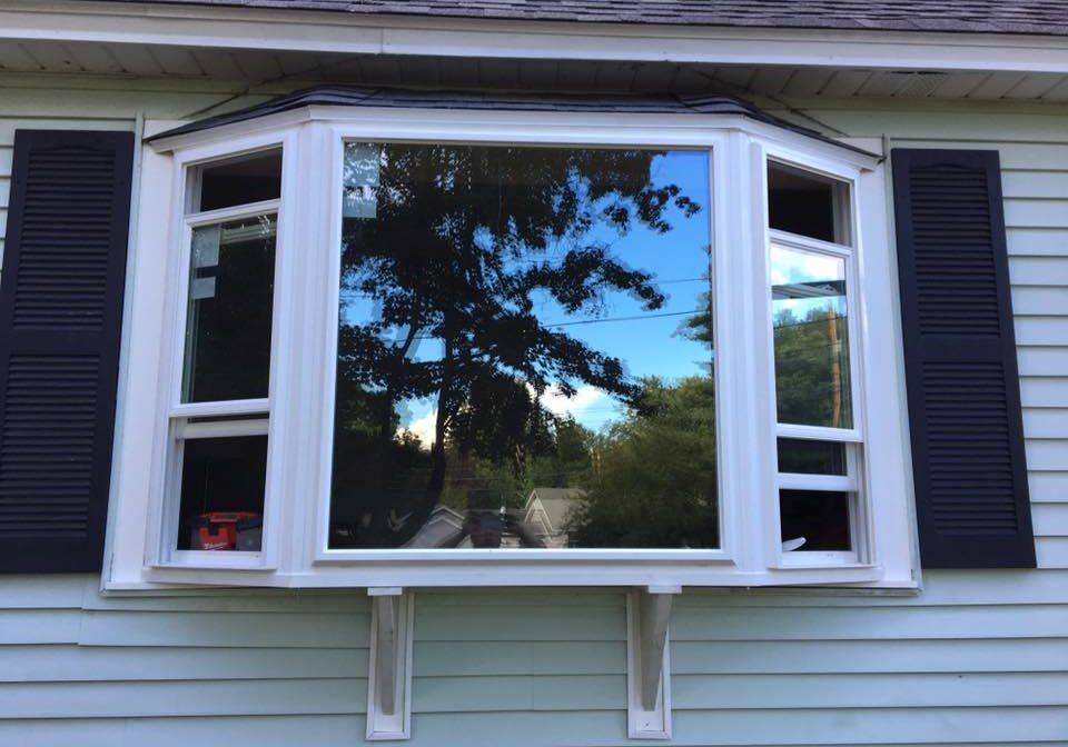 A large bay window reflecting a tree and sky.
